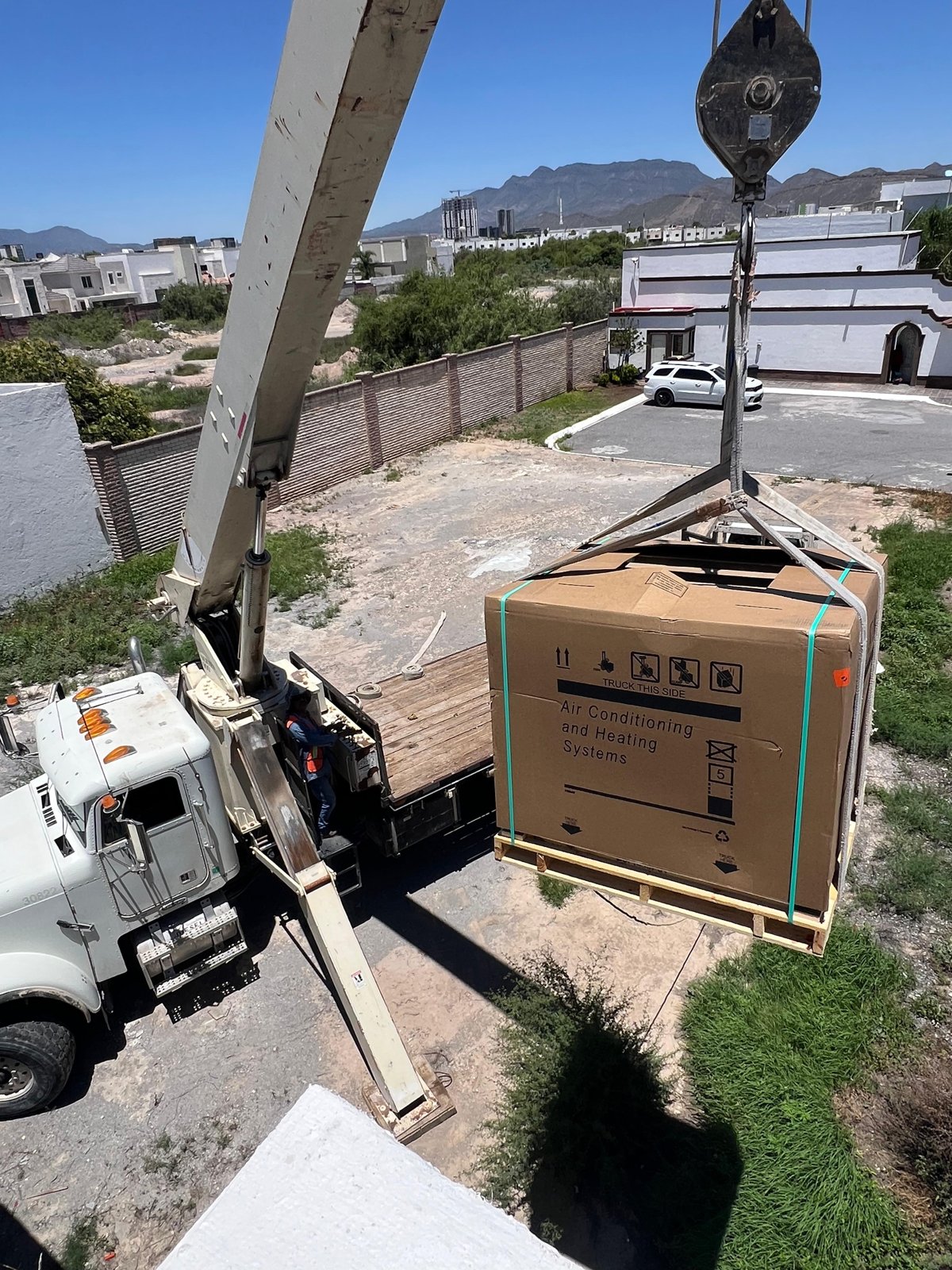 Grúa izando equipo de aire acondicionado a fraccionamiento residencial