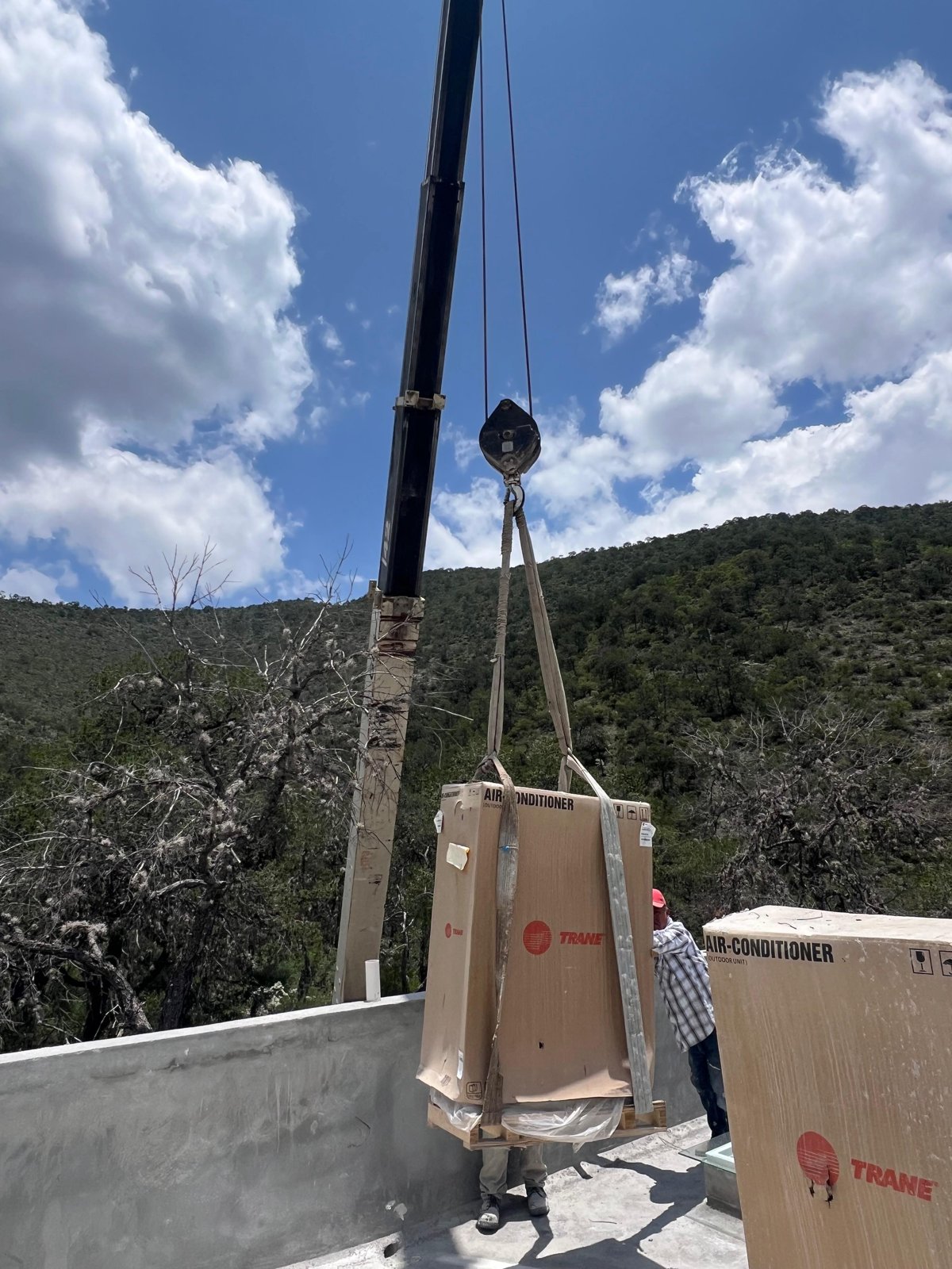 Grúa izando unidad de aire acondicionado Trane en zona montañosa